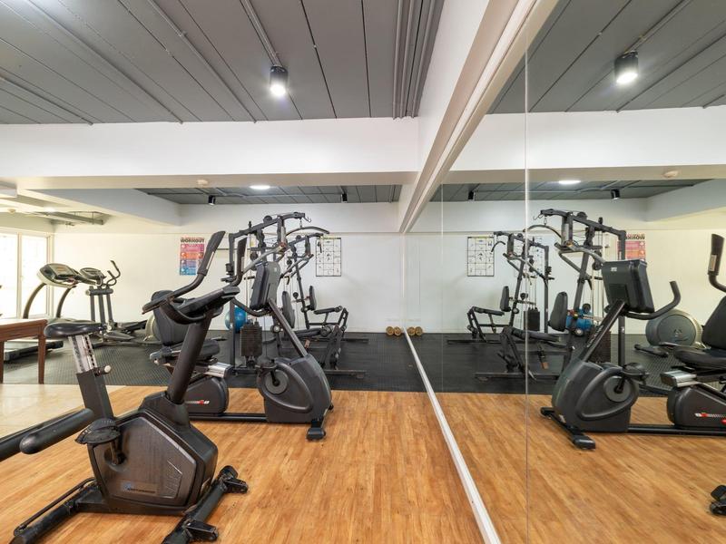 Fitnessraum mit verschiedenen Trainingsgeräten und Spiegelwand im Hotel.