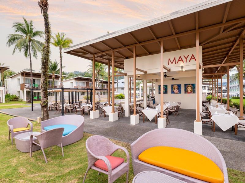 Offener Außenbereich einer Hotelbar mit Sitzgelegenheiten und Palmen bei Sonnenuntergang.