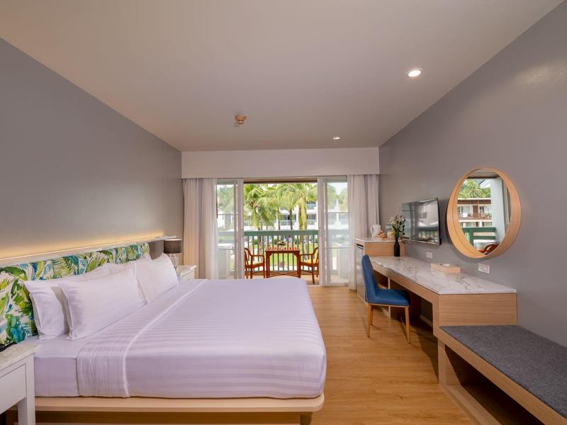 Modernes Hotelzimmer mit Kingsize-Bett, Schreibtisch, Spiegel und Zugang zu einem Balkon mit Aussicht auf Bäume.