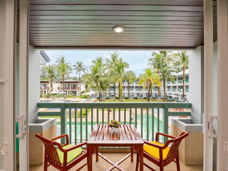 Blick von einem Balkon mit Tisch und zwei Stühlen auf einen Pool und Palmen.