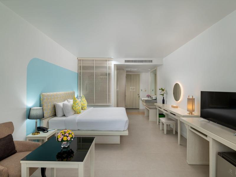 Modernes Hotelzimmer mit Doppelbett, Sitzbereich, Fernseher und Schreibtisch in neutralen Farben.