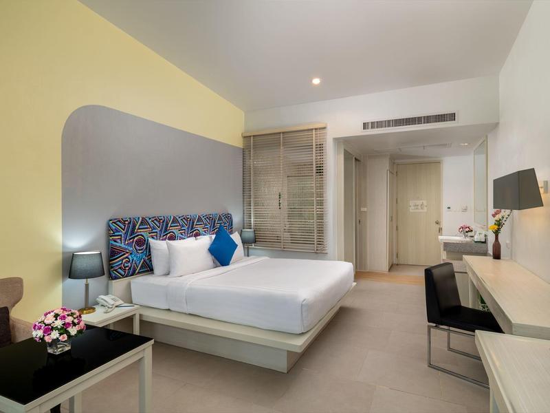 Modern eingerichtetes Hotelzimmer mit großem Bett, Schreibtisch und Glastür zum Bad.