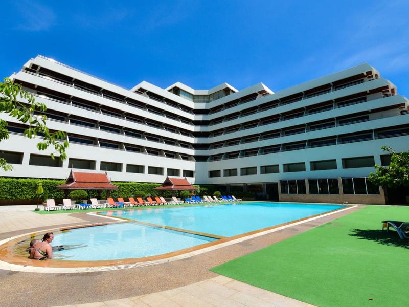 Complejo hotelero moderno con piscina al aire libre y sombrillas bajo cielo azul.