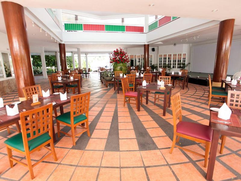 Amplio comedor de hotel iluminado con sillas de madera y decoración en mesas bajo ventanas y techo alto.