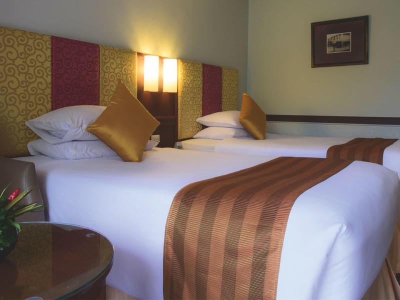 Habitación de hotel acogedora con dos camas, luz cálida y arreglo floral decorativo.