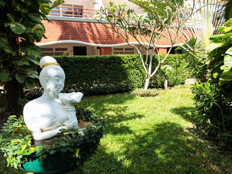 Área de jardín con césped verde, plantas y una estatua blanca.