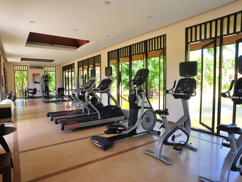 Salle de sport lumineuse avec tapis de course et vélos d'appartement à côté de grandes fenêtres donnant sur la verdure.
