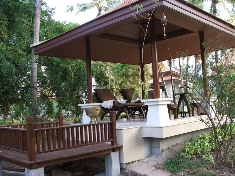 Terrasse couverte avec chaises en bois et table dans un jardin d'hôtel.