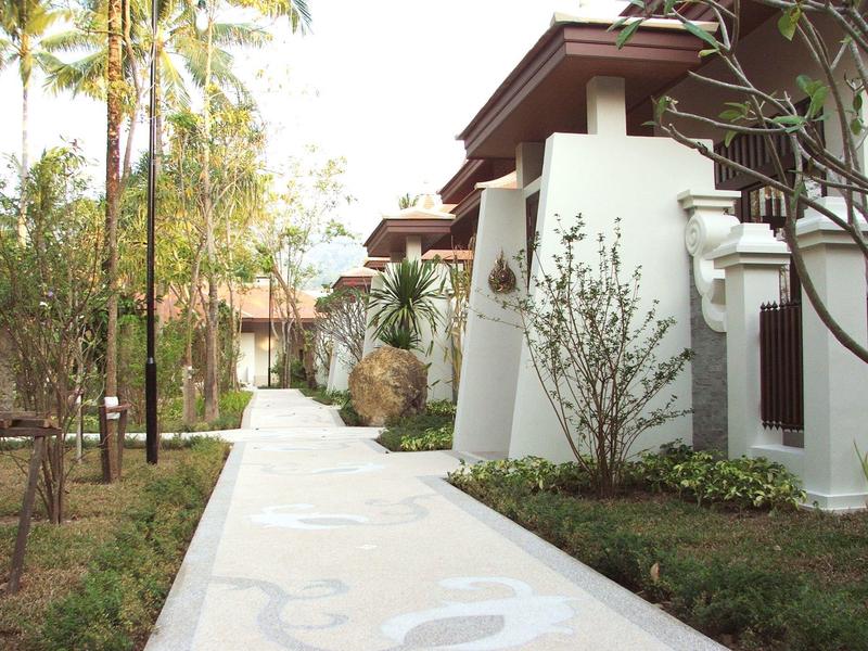 Un chemin pavé à côté d'un bâtiment blanc moderne avec jardin vert et palmiers.