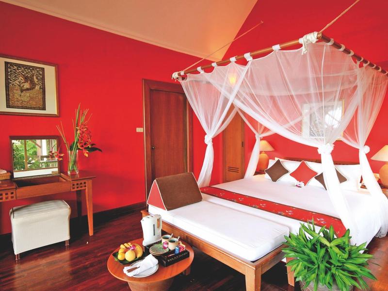 Helles Schlafzimmer mit roter Wand, Himmelbett mit weißem Baldachin und Holzmöbeln.