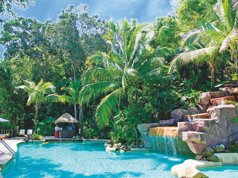 Ein tropischer Pool mit Wasserfall, umgeben von grünen Palmen und dichter Vegetation.