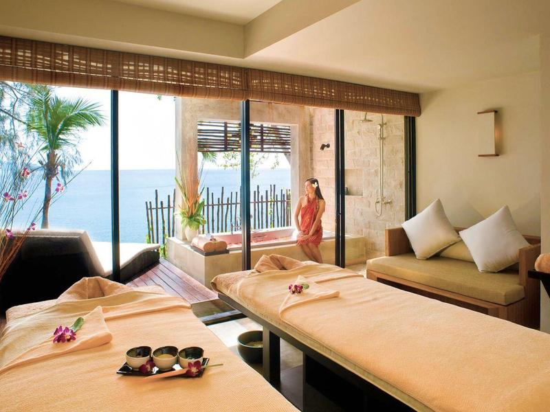 Helle Wellness-Lounge mit Massagebetten, Sofa, großen Fenstern und Blick aufs Meer.