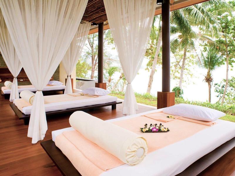 Offene Wellness-Liege mit weißen Vorhängen und grüner Gartenkulisse im Hintergrund.