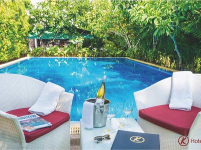 Pool mit blauen Wasser, umgeben von grünem Pflanzen, zwei weiße Stühle mit roten Kissen und Handtüchern.