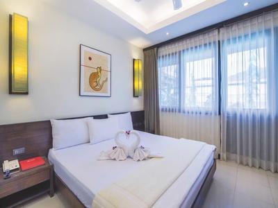 Helles Schlafzimmer mit großem Bett, Wandlampen und weißen Vorhängen am Fenster.