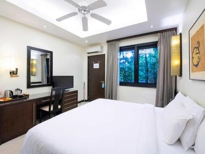 Helles Hotelzimmer mit großem Bett, Schreibtisch, Spiegel und Fenster mit Blick ins Grüne.