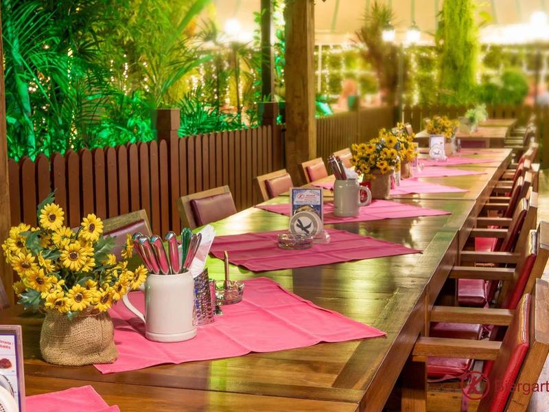 Langer Holztisch mit rosa Läufern, Sonnenblumen-Arrangements und Stühlen in hellem, warmem Licht.