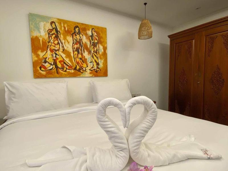 Zwei Handtücher geformt als Schwäne auf einem weißen Bett mit Blumen davor in einem Hotelzimmer.