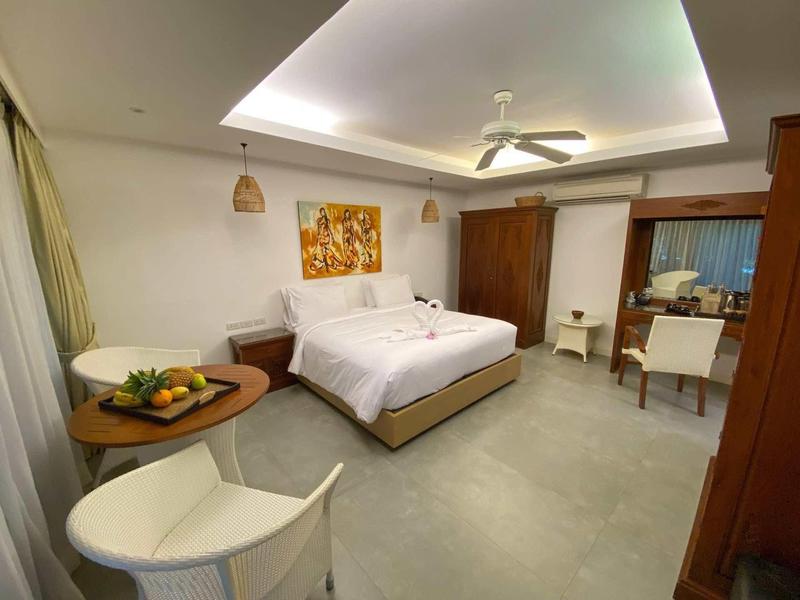 Modernes Hotelzimmer mit großem Bett, Deckenventilator, Sitzecke und indirekter Beleuchtung.