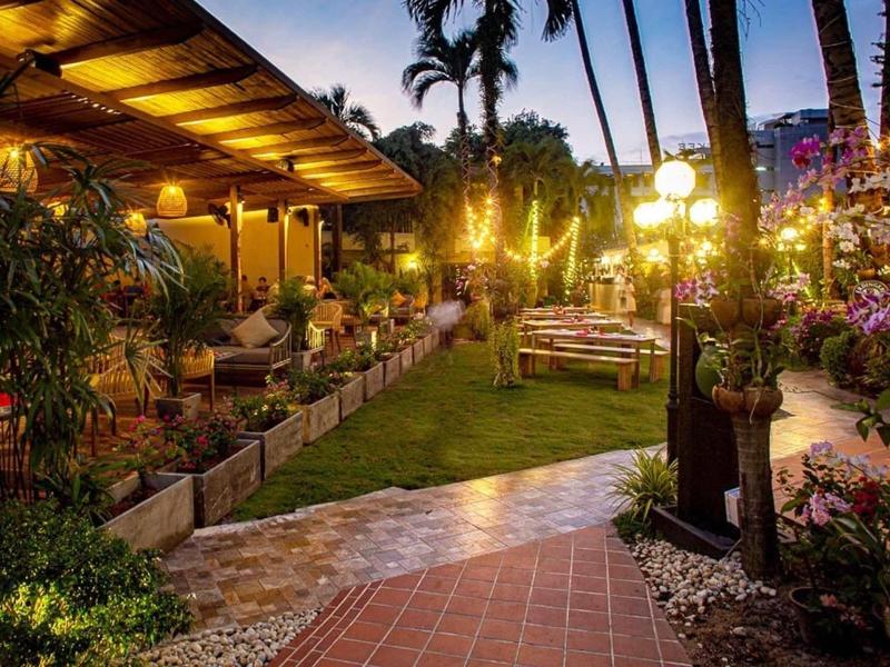 Abendliche Gartenlounge mit Holzmöbeln, warmen Lichtern und tropischen Pflanzen bei Dämmerung.