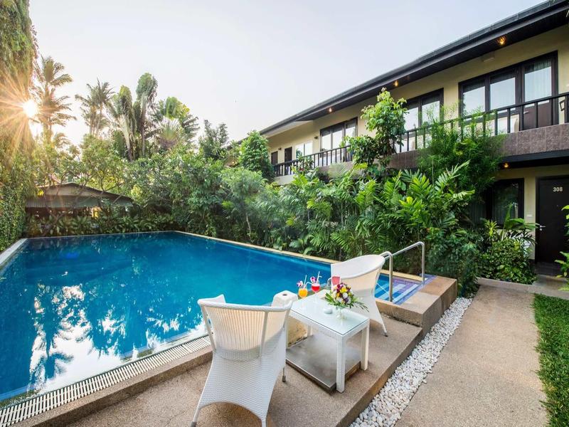 Moderner Außenpool mit Liegestühlen, Blumen und zweistöckigem Gebäude im Hintergrund bei Sonnenlicht.