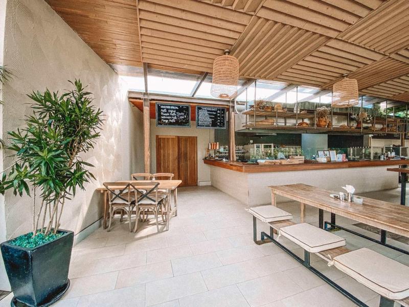 Helles modernes Café mit Holzdecken, großen Pflanzen und Holz-Tischen mit Sitzkissen.