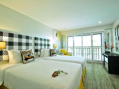 Hell eingerichtetes Zimmer mit zwei Doppelbetten, großem Fenster, gelbem Sessel und dunklem Sideboard.