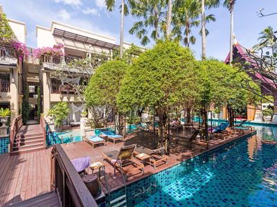 Moderner Außenpool mit blauen Fliesen, Liegestühlen, Bäumen und Palmen in einem Hotelkomplex.