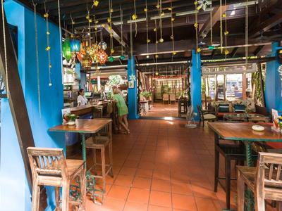 Innenraum eines Restaurants mit Holztischen, blauen Vorhängen und Terrakottafliesenboden.