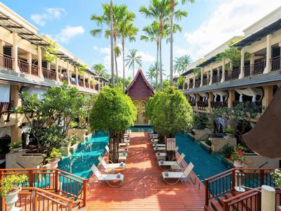 Dziedziniec hotelu z basenami, leżakami między dwoma skrzydłami budynków i palmami.