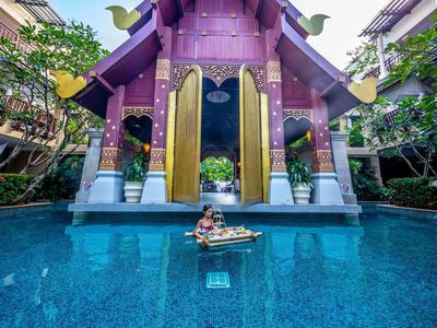 Ein Mädchen sitzt in einem traditionellen Boot auf blauem Wasser vor einem lila Tempel mit goldenen Türen.