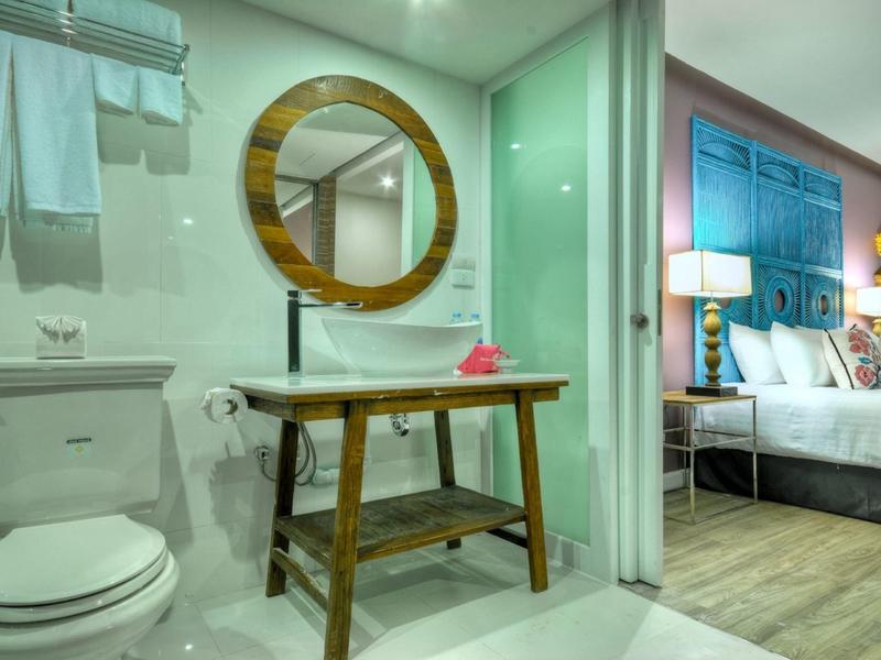 Modernes Badezimmer mit rundem Holzspiegel, Holzwaschtisch und angrenzendem Schlafzimmer mit blauen Möbeln.