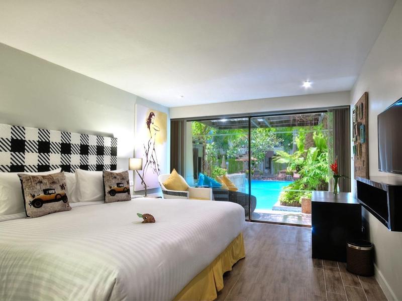 Modernes Hotelzimmer mit großem Bett, TV, Schreibtisch und Blick auf einen Pool im Grünen.