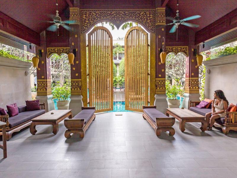 Offener Wohnbereich mit Holzsofas, Kissen und großen vergoldeten Türen, Blick auf Garten und Pool.