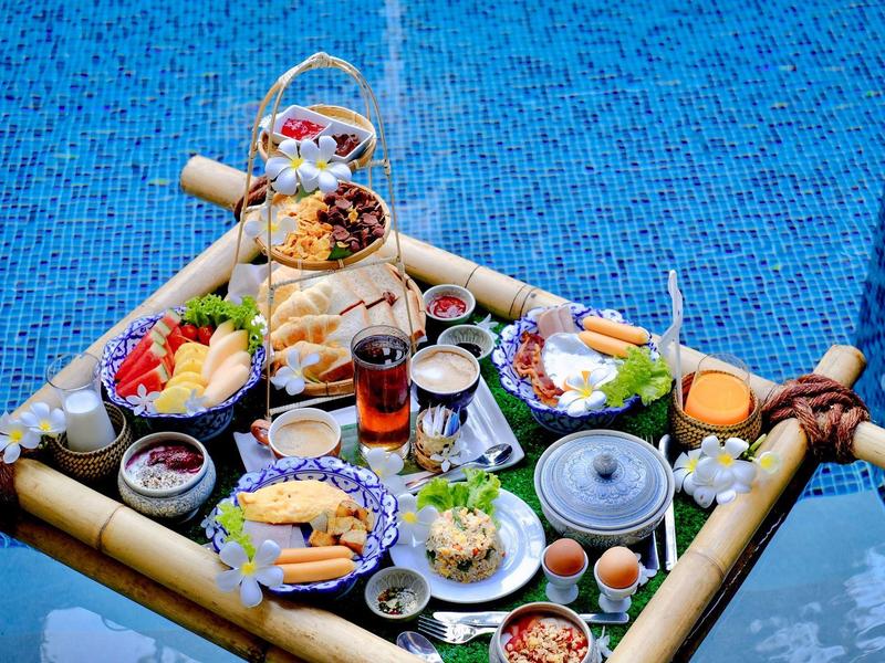 Vielseitiges Frühstück mit Obst, Eiern, Getränken und anderen Speisen auf Bambustablett im Pool.