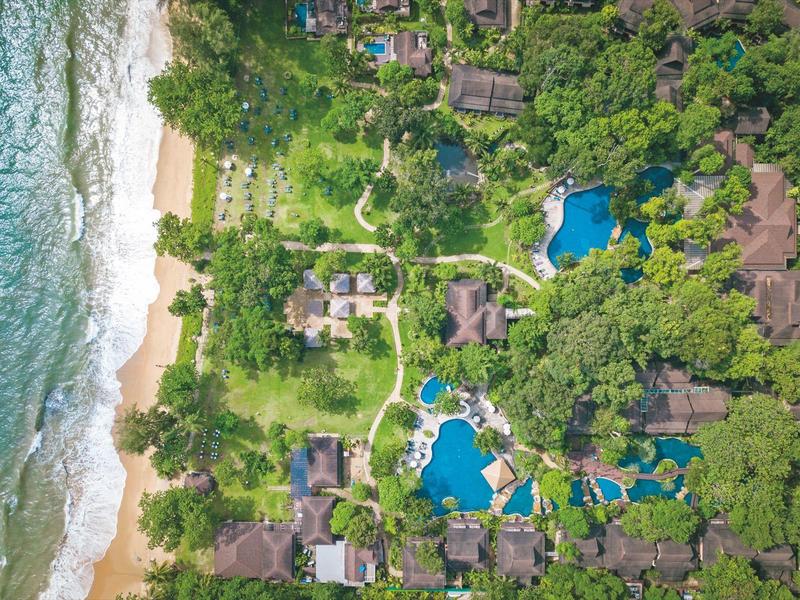 Luftaufnahme eines Resorts am Strand mit mehreren Pools, umgeben von dichtem Grün.