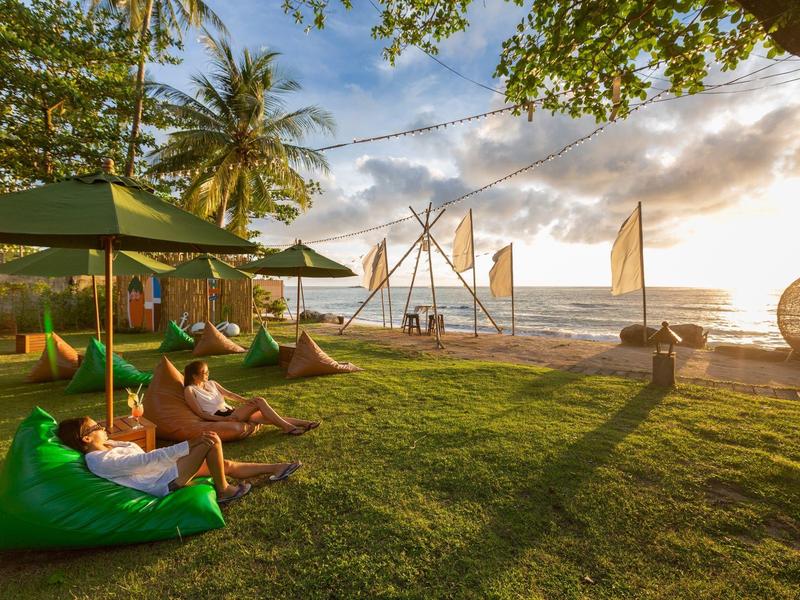 Menschen entspannen auf grünen Sitzsäcken am Strand bei Sonnenuntergang.