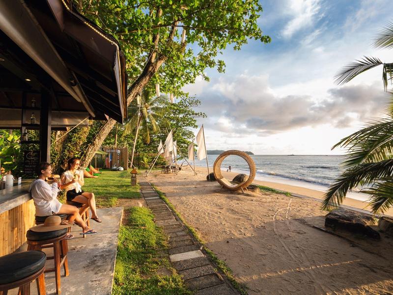 Strandbar mit Sitzgelegenheiten am Sandstrand und Blick aufs Meer bei Sonnenuntergang.