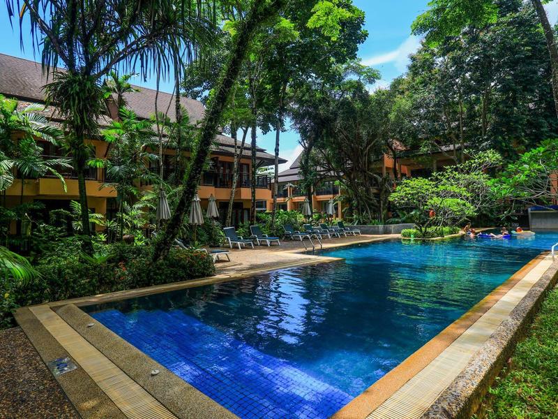 Ein blauer Außenpool umgeben von tropischer Vegetation und Gebäuden unter blauem Himmel.