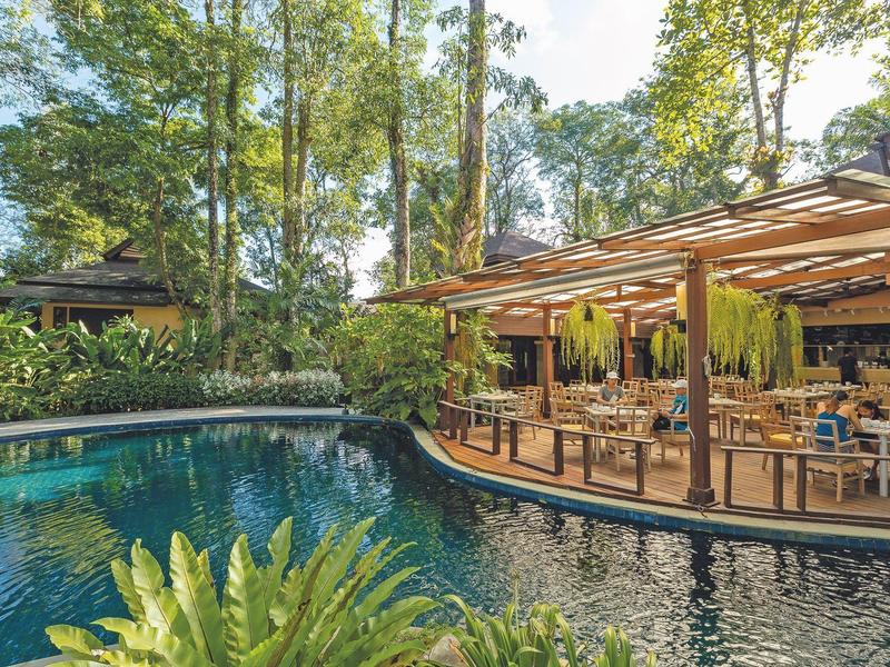 Gemütliches Restaurant mit Terrasse neben einem Wasserbecken und umgeben von Bäumen.