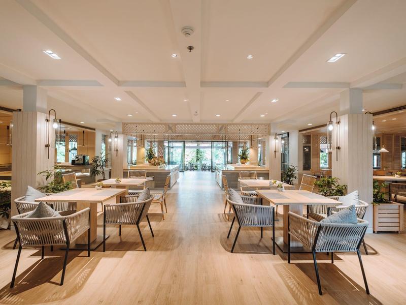 Moderner, heller Frühstücksbereich mit Tischen, Stühlen und großem Fenster am Ende des Raumes.