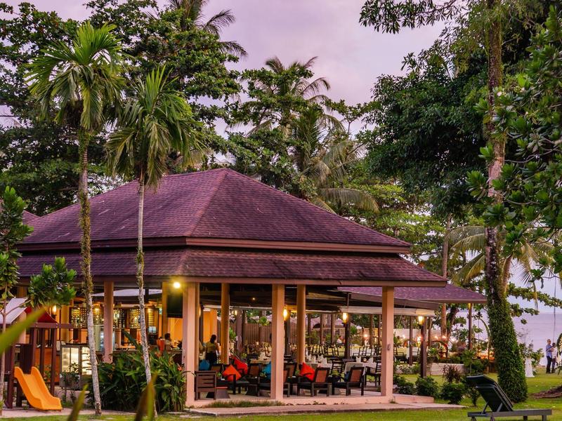 Ein Pavillon mit offenem Restaurantbereich umgeben von Palmen und grüner Landschaft bei Sonnenuntergang.