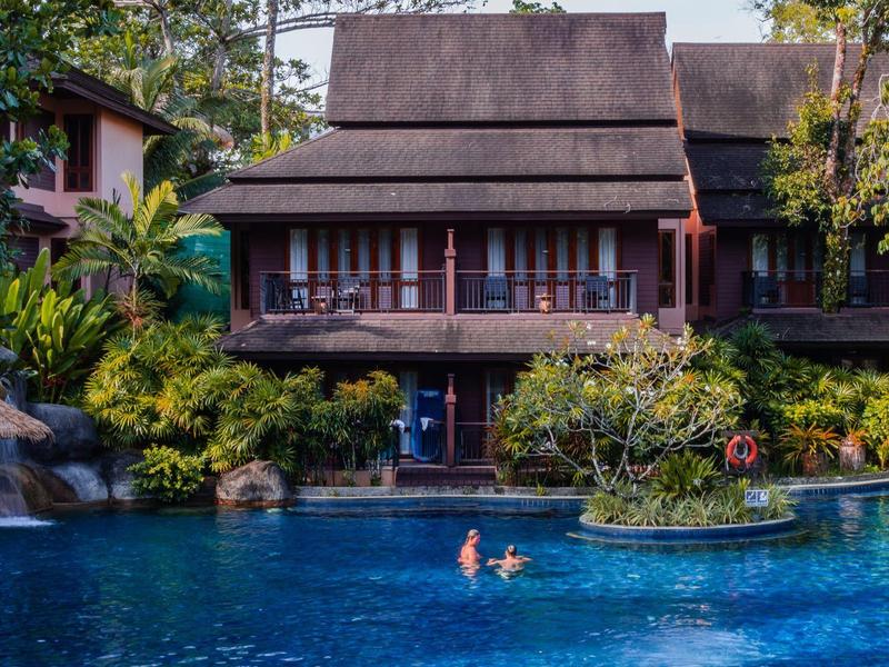 Ein Haus mit Veranda über einem Pool, umgeben von Bäumen und Pflanzen.