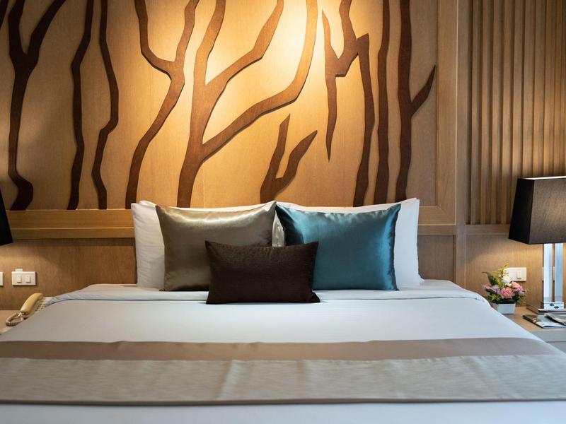 Modernes Hotelzimmer mit großem Bett, dekorativen Kissen und stilvoller Wandbeleuchtung.