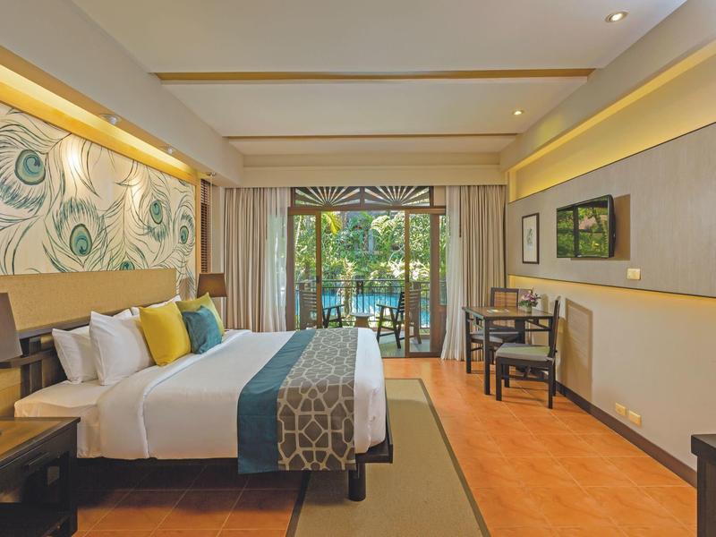 Modernes Hotelzimmer mit großem Bett, Schreibtisch, TV und Blick auf den Garten.