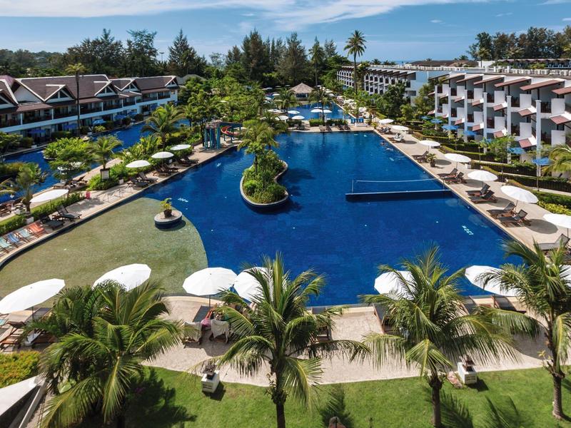 Großer Pool mit Sonnenschirmen, Palmen und mehrstöckigen Hotelgebäuden bei klarem Himmel.