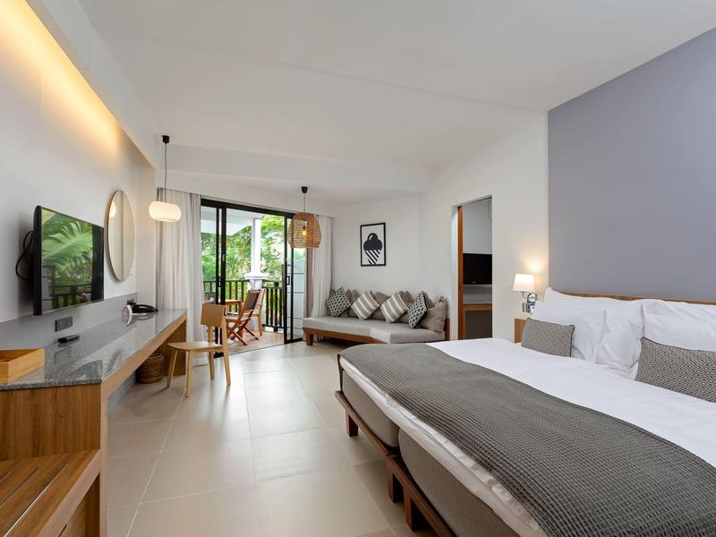 Modernes Hotelzimmer mit großem Bett, Sofa, TV und Balkon mit Aussicht im Tageslicht.