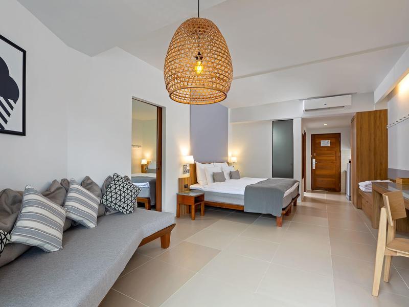 Modern eingerichtetes Hotelzimmer mit Bett, Sofa, Schreibtisch und stilvoller Beleuchtung.