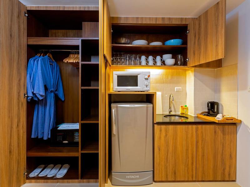 Kleiner Hotelküchenbereich mit Holzschränken, Mikrowelle, Kühlschrank und offenen Fächern mit Geschirr.