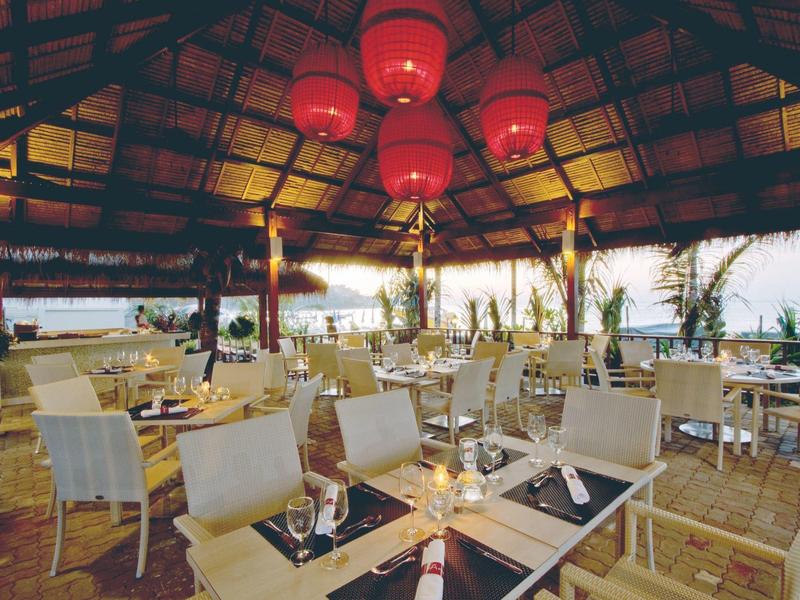 Offenes Restaurant mit weißen Stühlen, Holzdach und Blick auf das Meer.